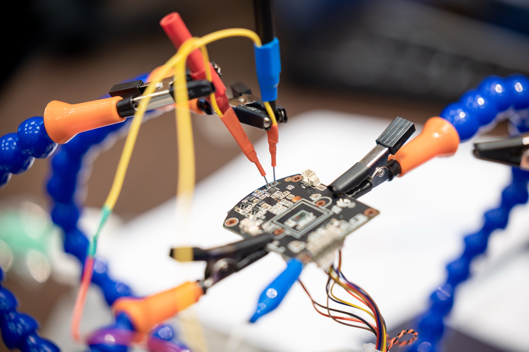 Vantage Point IoT hardware testing bench, a connected device PCB held by helping-hands clamps with logic-probe pins making contact with debug pads under instrumentation.